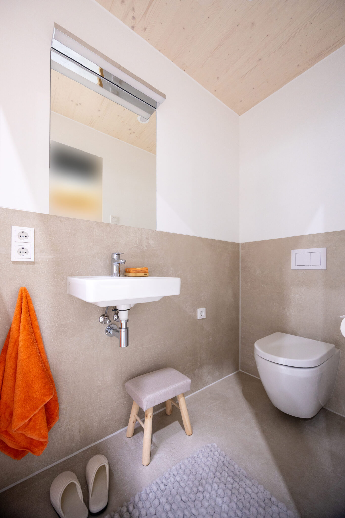 Tjiko-Badezimmer aus dem Projekt Murnau: beige Wandfliesen und orangefarbene Akzente.